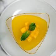 Top view of a mango jelly cup with chopped mango cubes and mint leaf garnish.