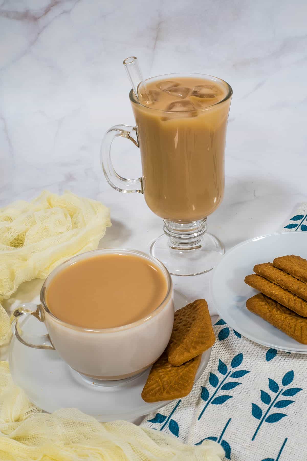 A glass of iced tea and a cup of hot tea with biscuits on the side.