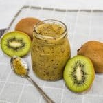 A bottle of kiwi coulis with kiwi fruits on the side.