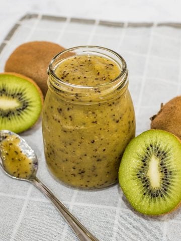 A bottle of kiwi coulis with kiwi fruits on the side.