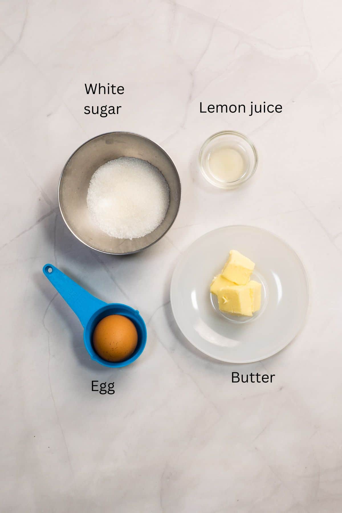 White sugar, butter, egg and lemon juice against a marble background.