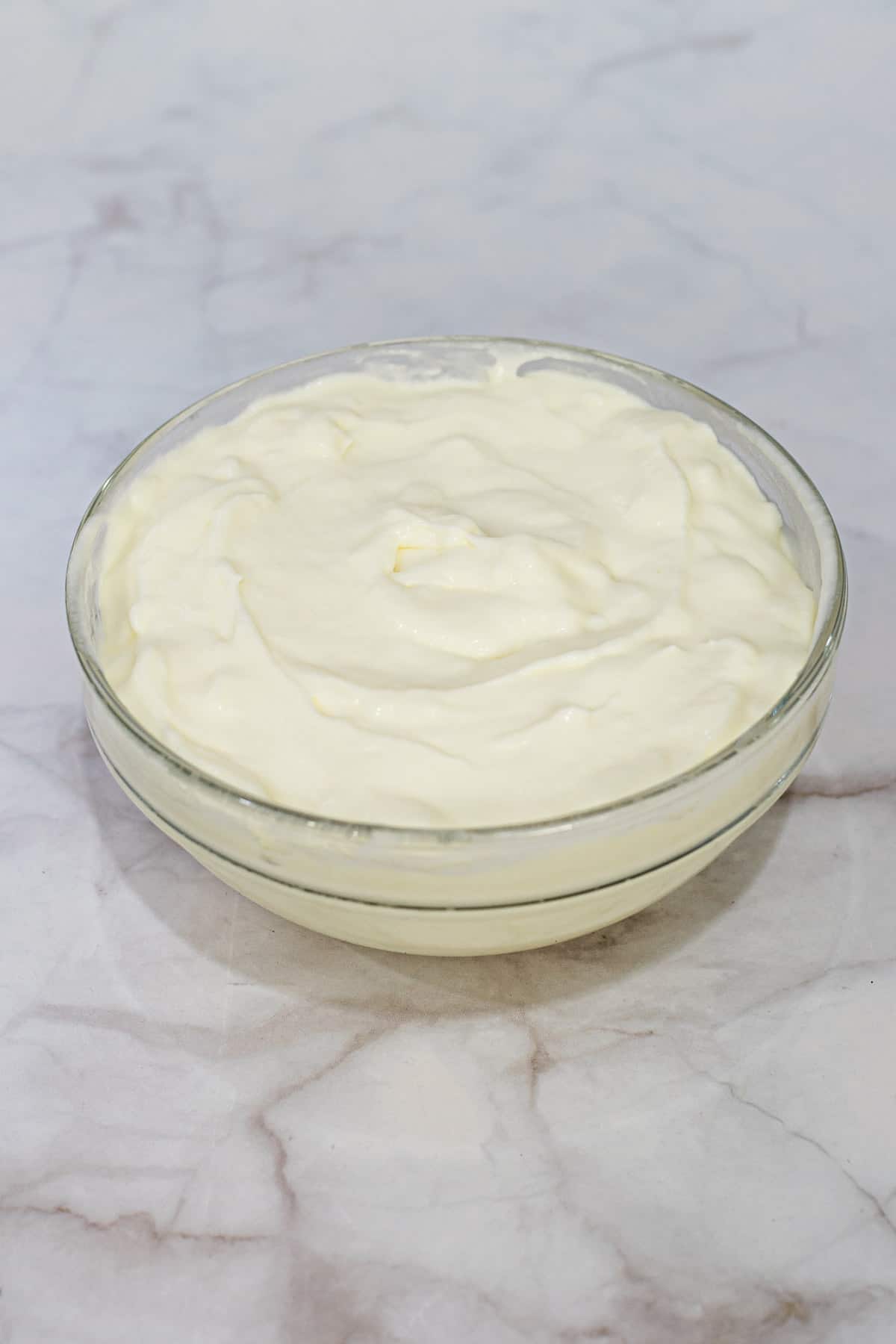 A bowl of mascarpone cheese against marble background.