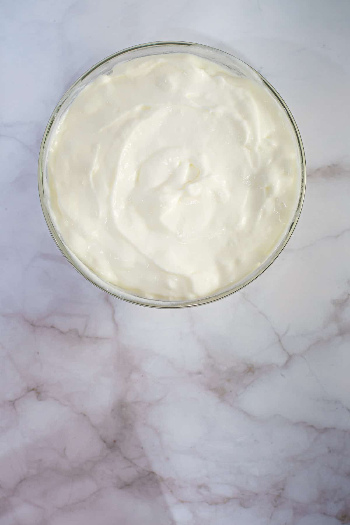 A bowl of mascarpone cheese against marble background.