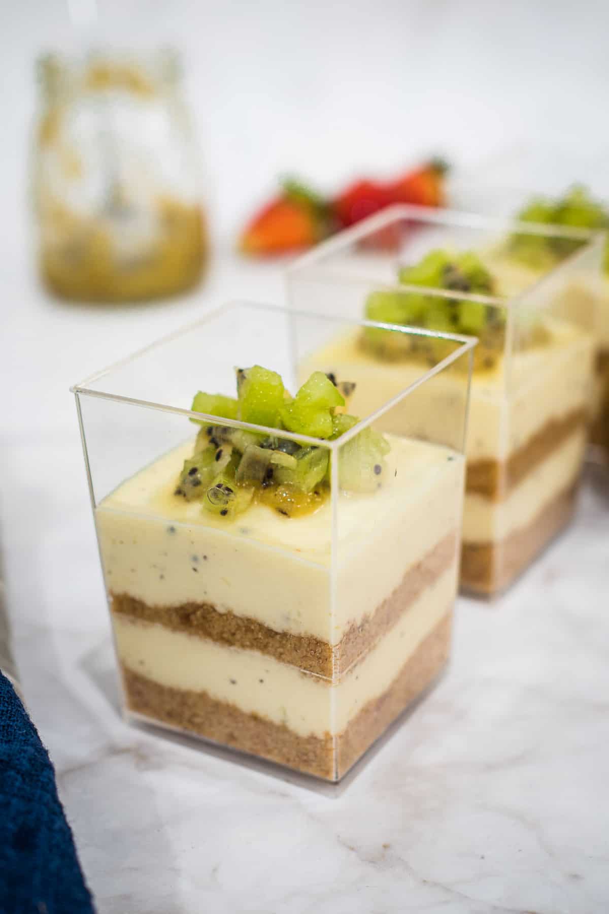 Kiwi cheesecake square cups with 2 layers of crumbs and 2 layers of cheese.