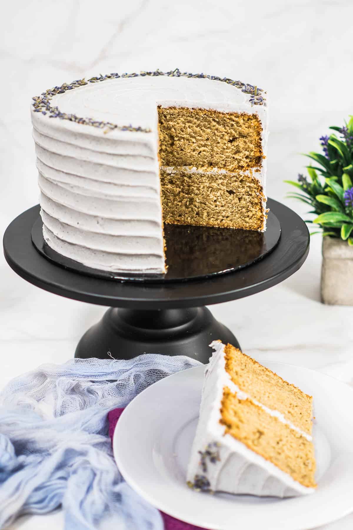 A two tier frosted cake on a black stand, with a large slice of cake cut out.