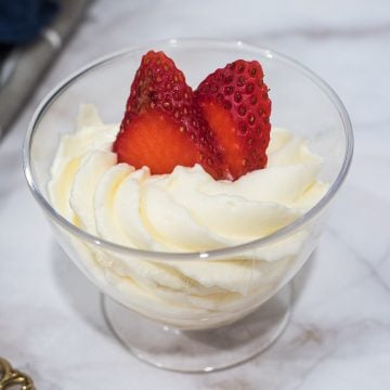 Mascarpone whipped cream frosting piped into a glass and decorated with strawberry slices.