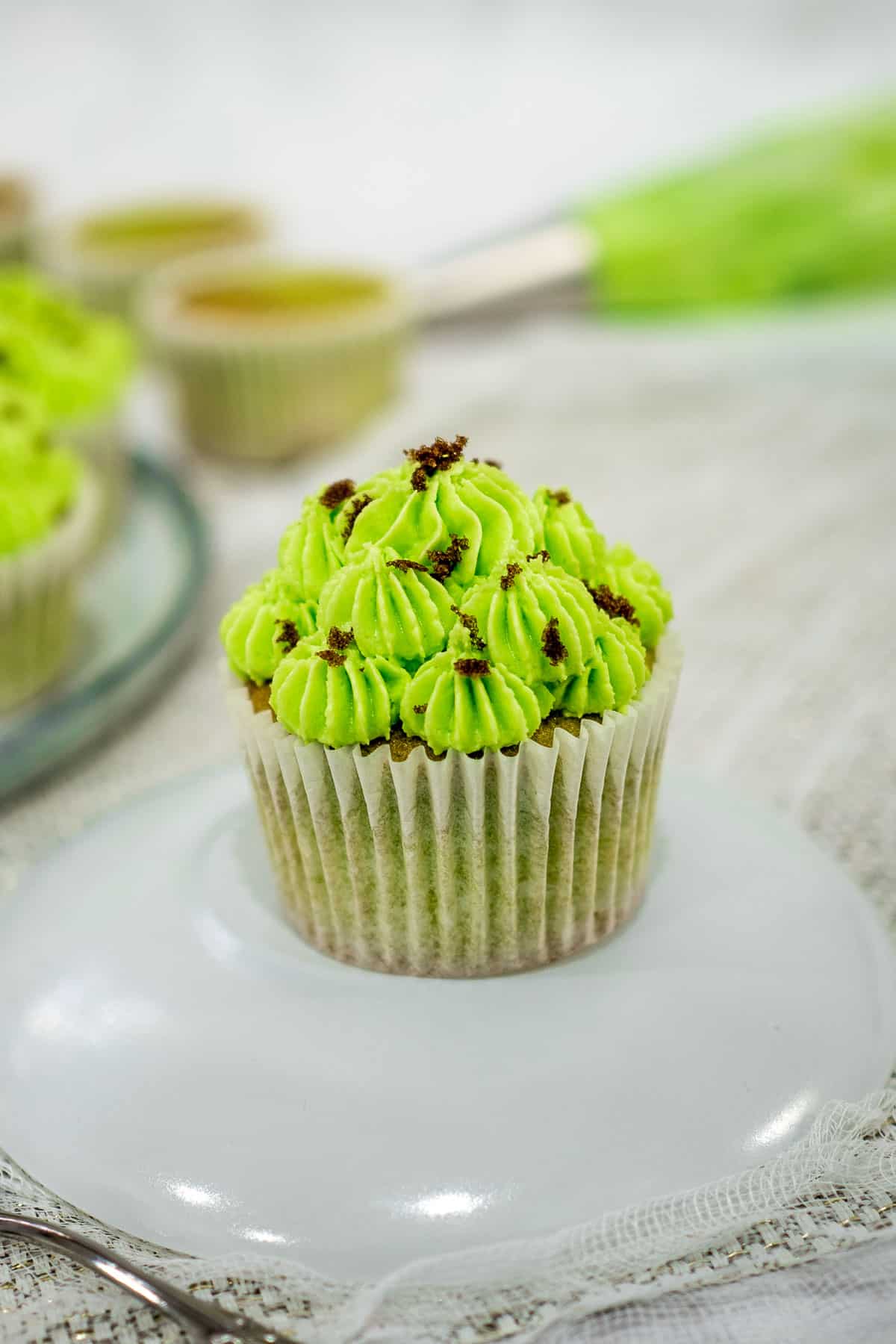 A green cupcake with green buttercream icing on a white plate.