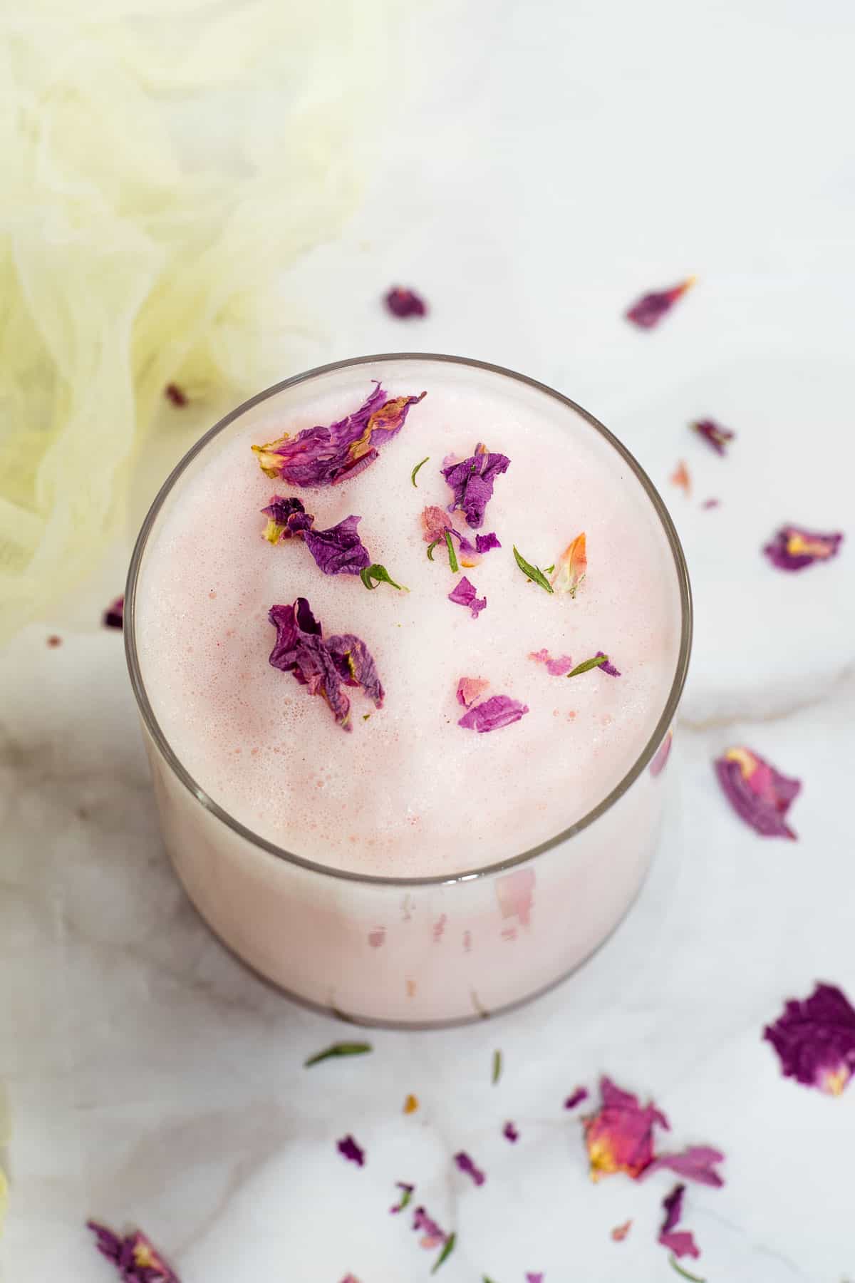 A glass of rose milk with rose petal flakes on top.