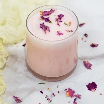 A glass of rose milk with rose petal flakes on top.