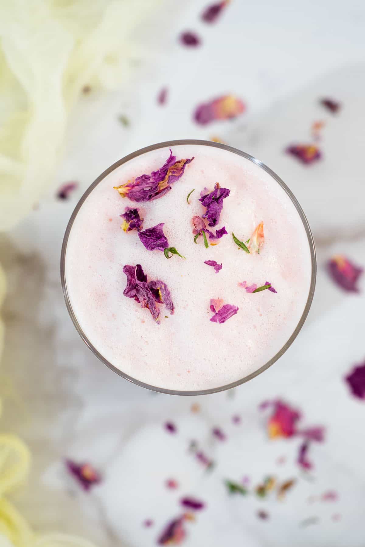 Top view of a glass of pink milk with pink rose flakes.