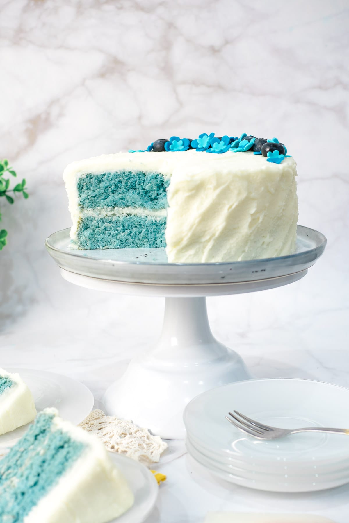 A blue cake with white frosting on a white cake stand, with a few slices cut out onto white plates.