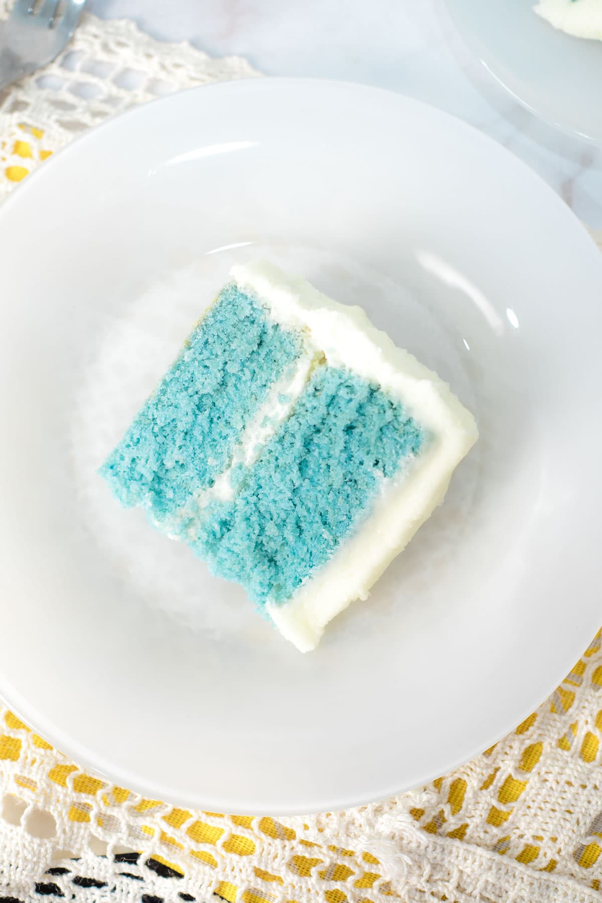 A slice of blue cake with white frosting on a white plate.