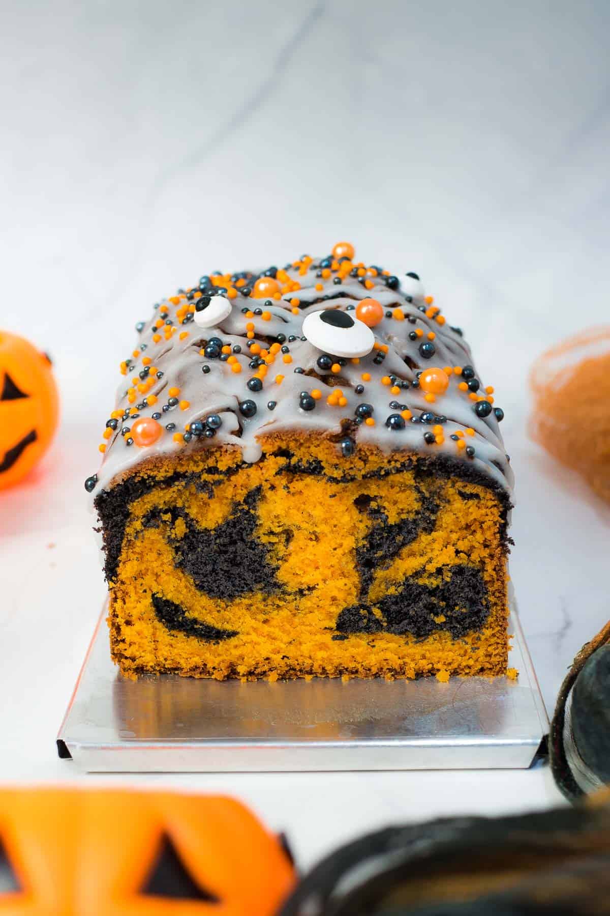 An orange and black marble loaf cake with white glaze and orange and black and eyeball candy sprinkles.