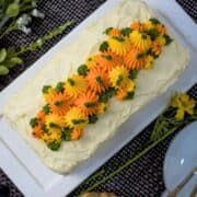 A loaf cake covered in cream cheese frosting and decorated with orange and yellow piped pumpkins and green leaves.