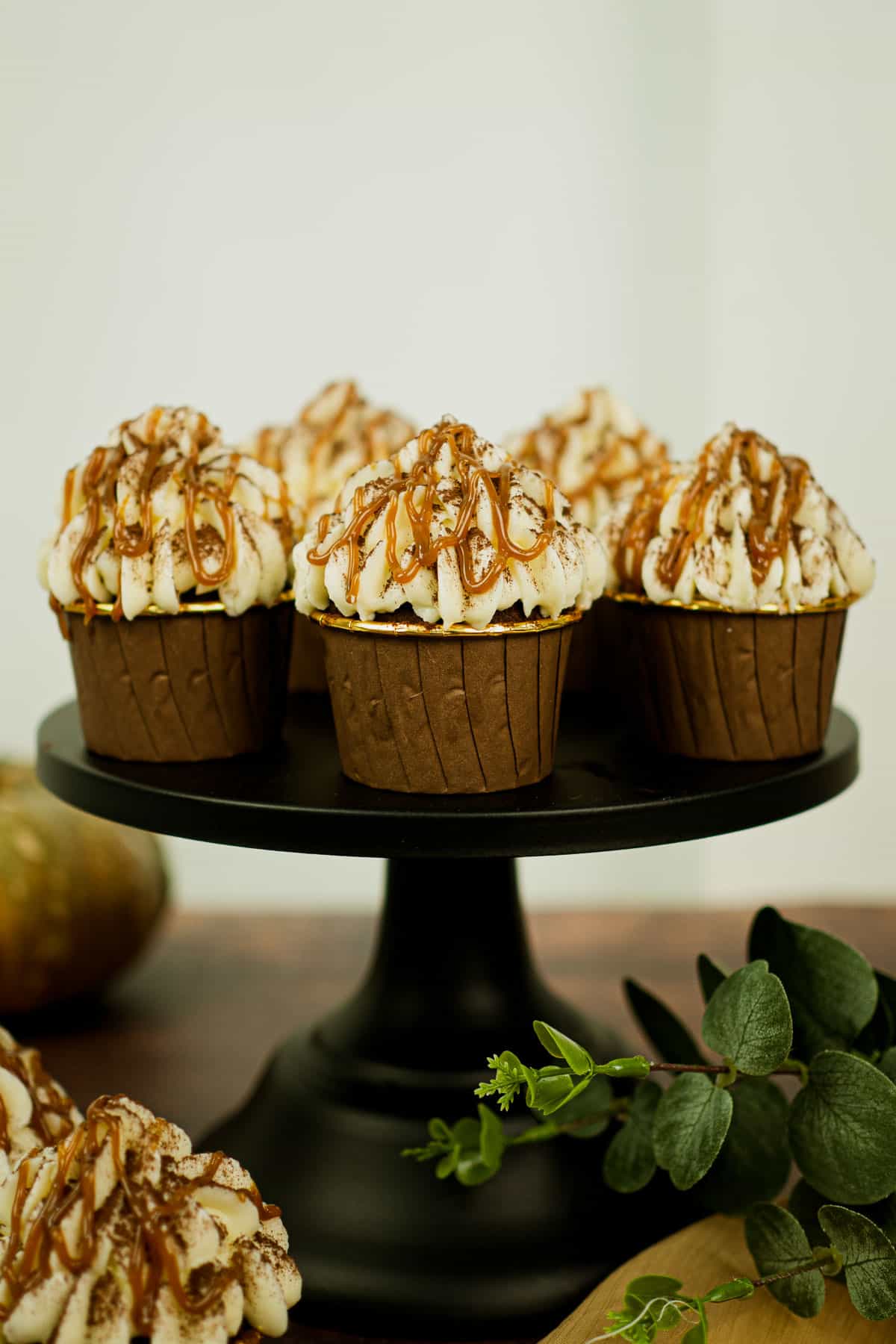 Cupcakes with caramel drizzle in brown muffin cups on a black cake stand.