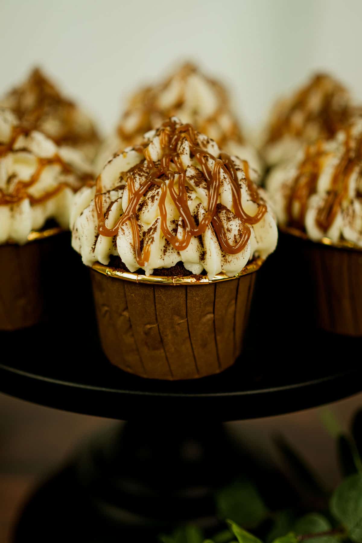 Chocolate cupcakes in chocolate casings topped with cream cheese frosting and caramel drizzle.