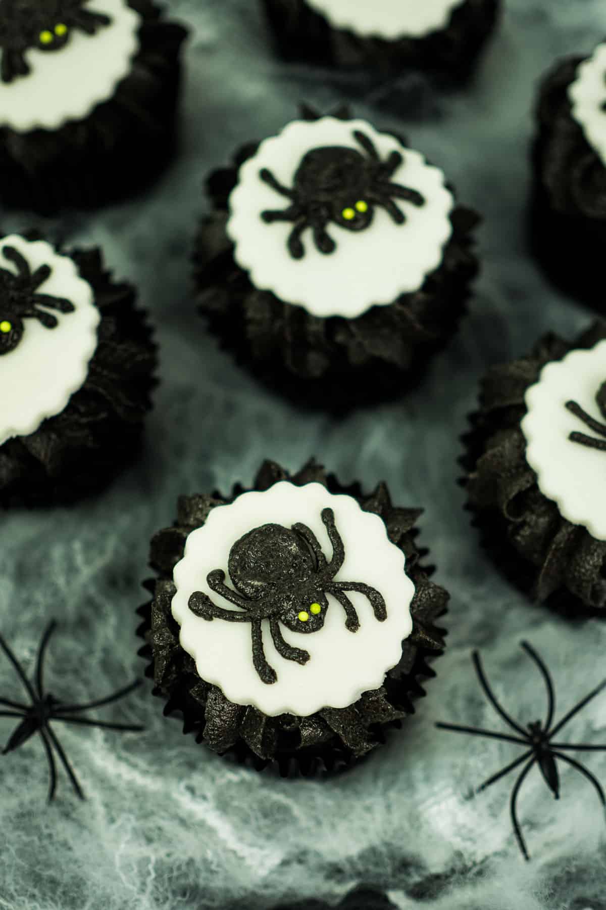 Chocolate cupcakes in black cupcake liners, decorated with black frosting, white fondant cut out and black buttercream spiders.