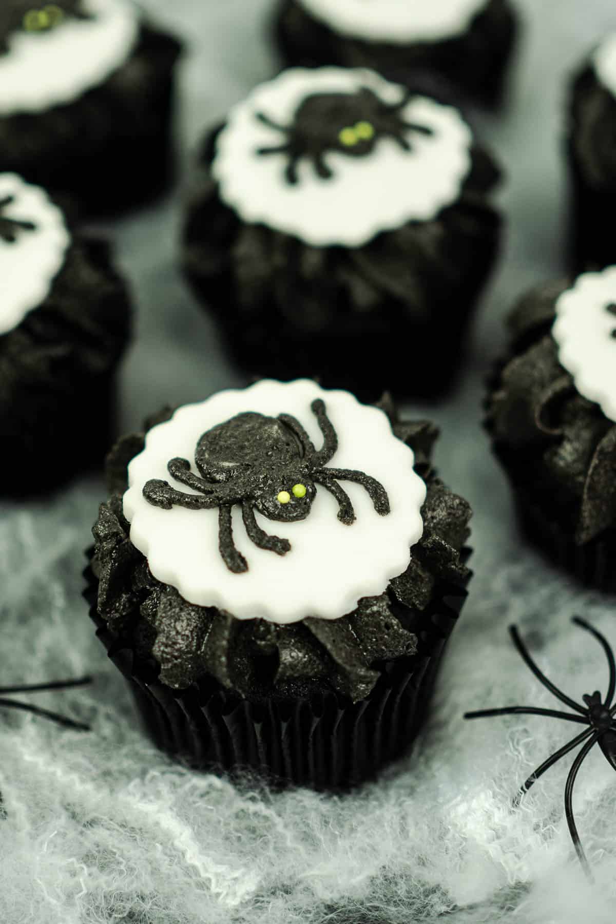 Chocolate cupcakes in black cupcake liners, decorated with black frosting, white fondant cut out and black buttercream spiders.