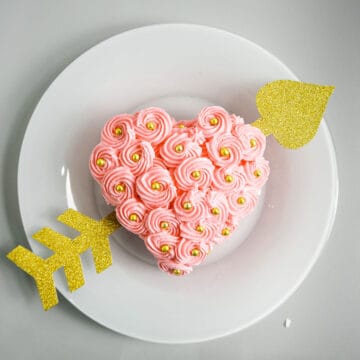 A pink heart shaped cake with buttercream rosette frosting and gold arrow running across.