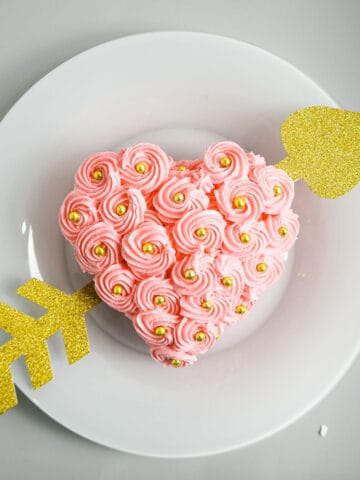 A pink heart shaped cake with buttercream rosette frosting and gold arrow running across.