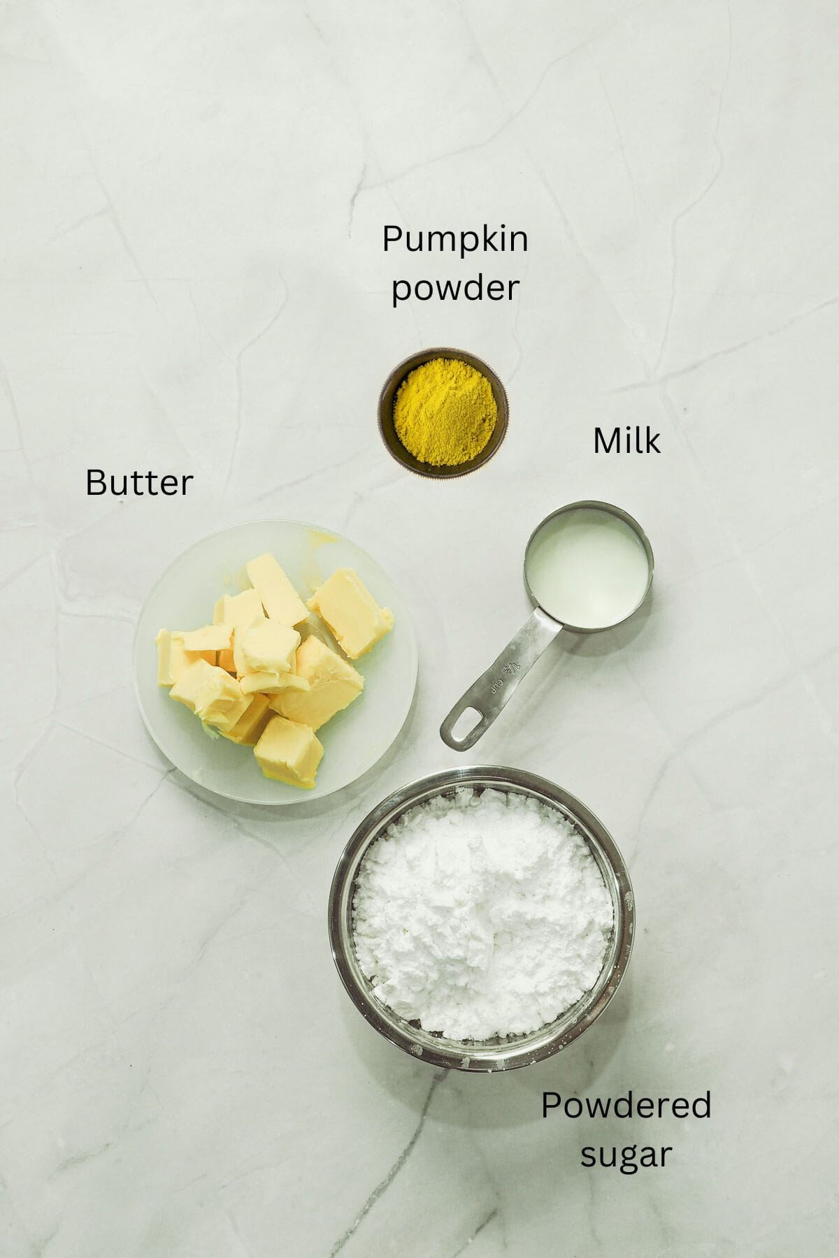 Powdered sugar, butter, milk and pumpkin powder against a marble background.