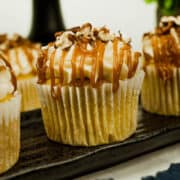 Pumpkin cupcakes with white frosting, caramel drizzle and chopped pecans on a brown plate.