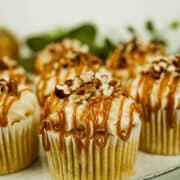 Pumpkin cupcakes with cream cheese frosting, caramel sauce drizzle sauce and chopped pecan topping on a grey plate.