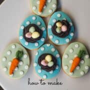 Egg shaped cookies in blue with 3D bird nest and 3 fondant eggs and egg shaped cookies in green with fondant carrot toppers.
