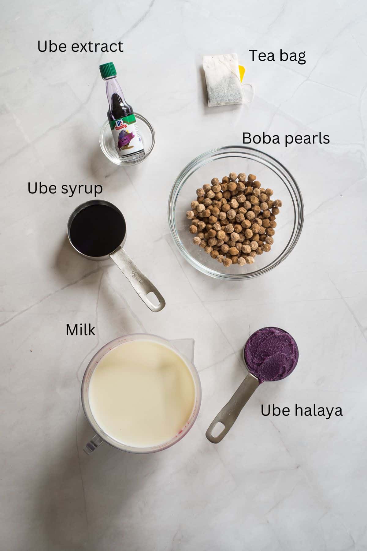 Tea bag, boba pearls, ube halaya, milk, ube syrup and ube extract against marble background.