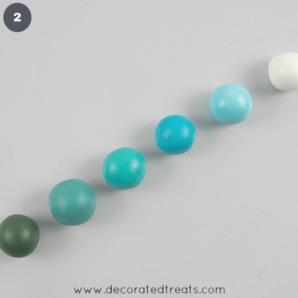 Six balls in deep green, dark turquoise, turquoise, dark blue, light blue and white arranged in a row.
