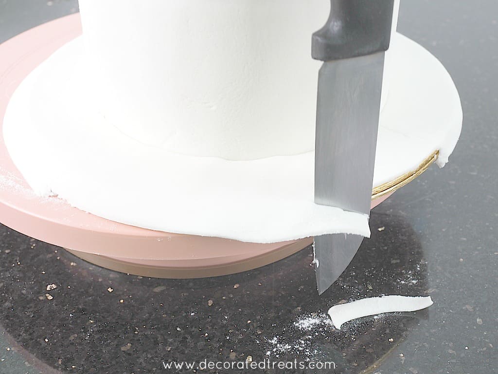Trimming excess fondant off a cake board.