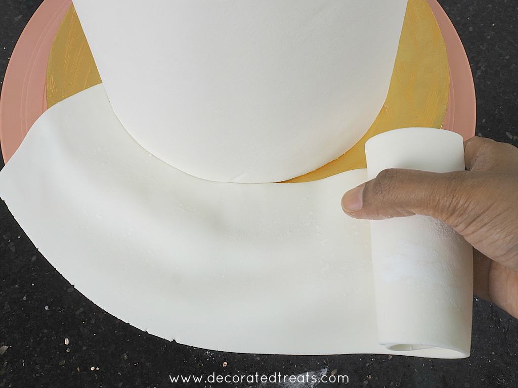 Covering a cake board with white fondant.