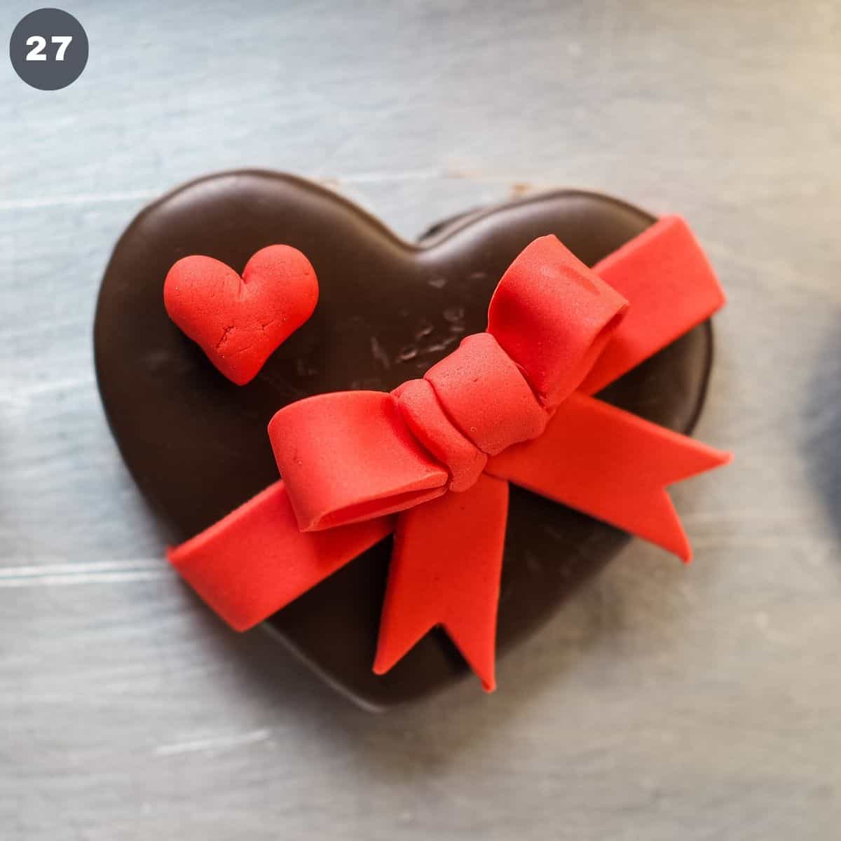 A chocolate cookie decorated with red fondant heart and bow.