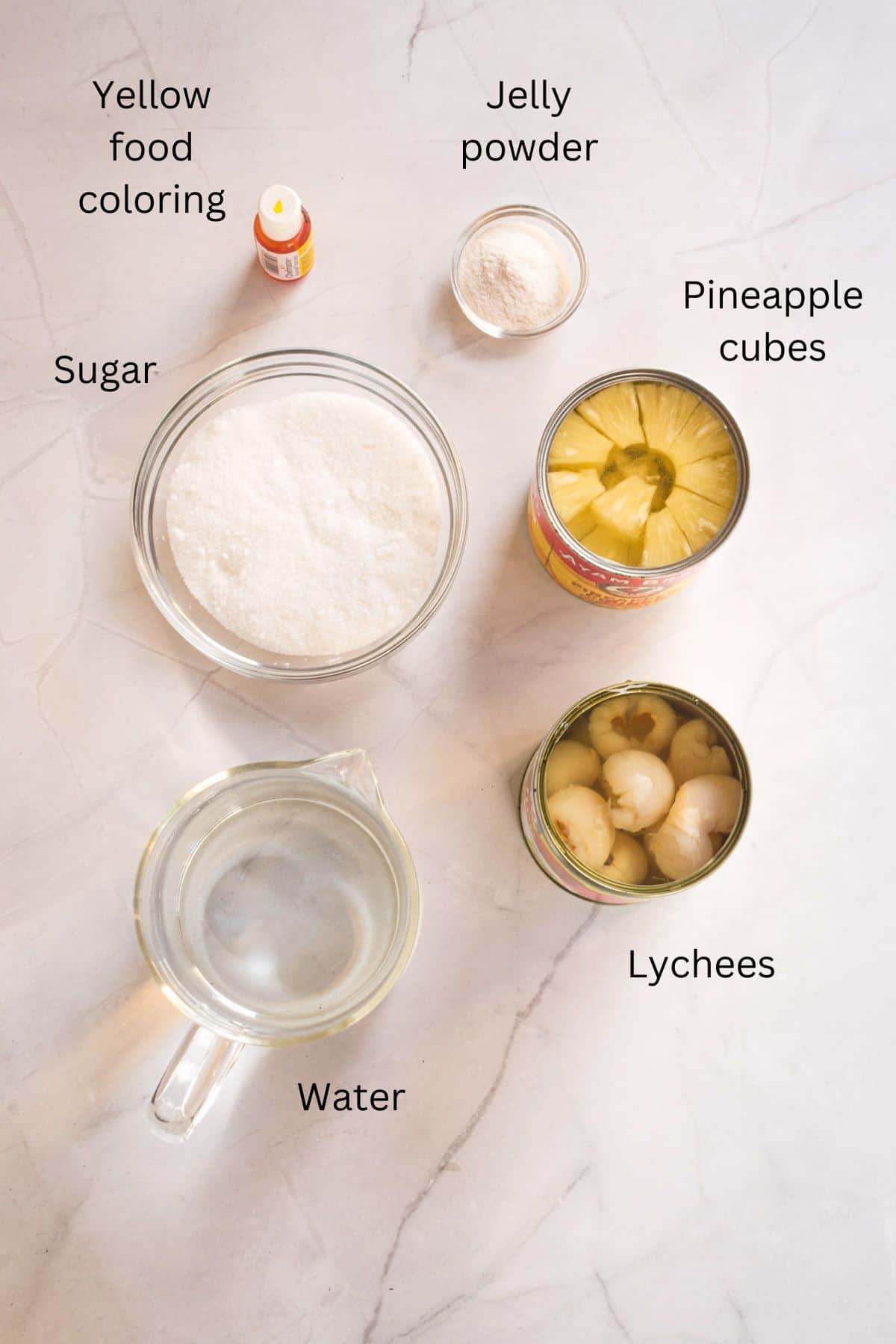 Lychees, pineapple cubes, water, sugar, jelly powder and yellow food coloring against a marble background.