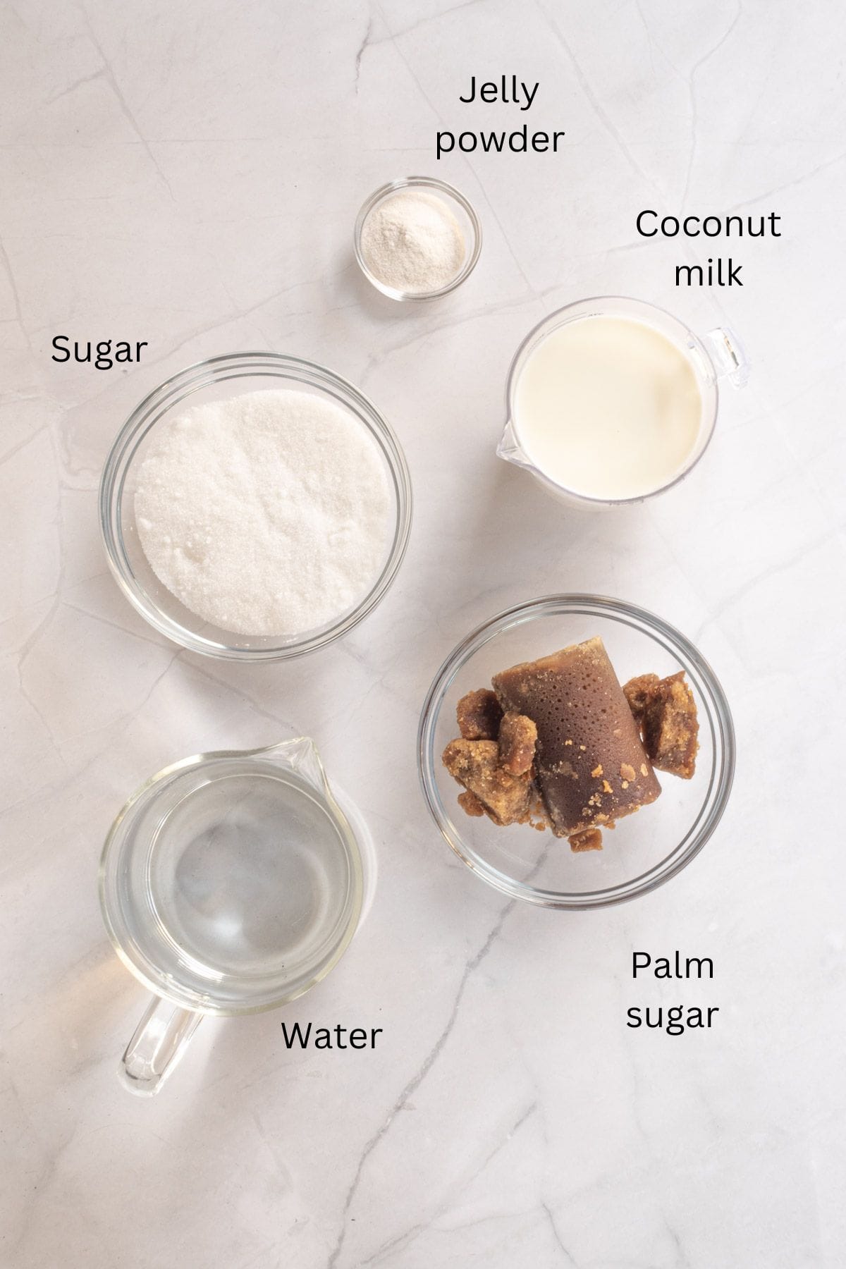 Agar agar powder, gula melaka (palm sugar), water, sugar and coconut milk against a marble background.