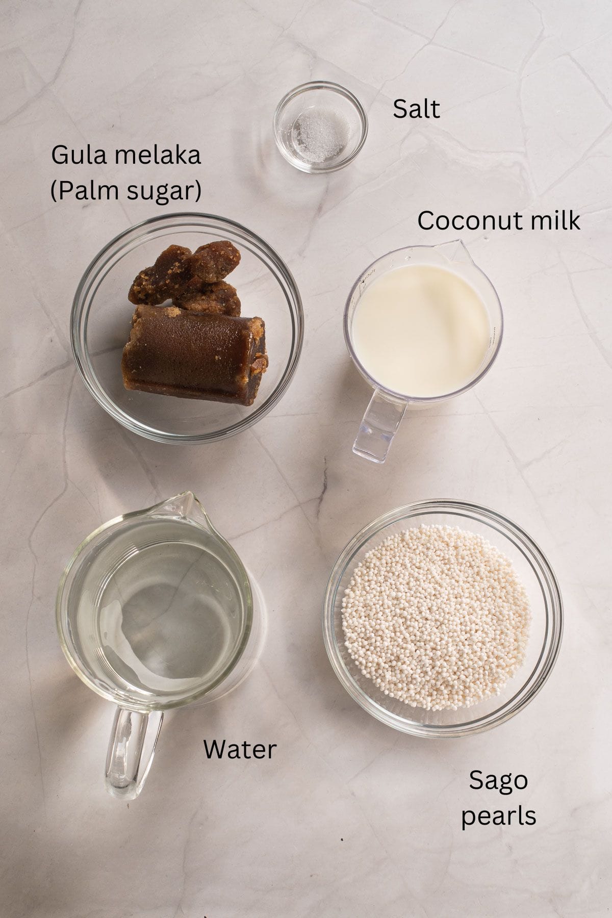 Gula melaka, water, salt, sago and coconut milk against a marble background.